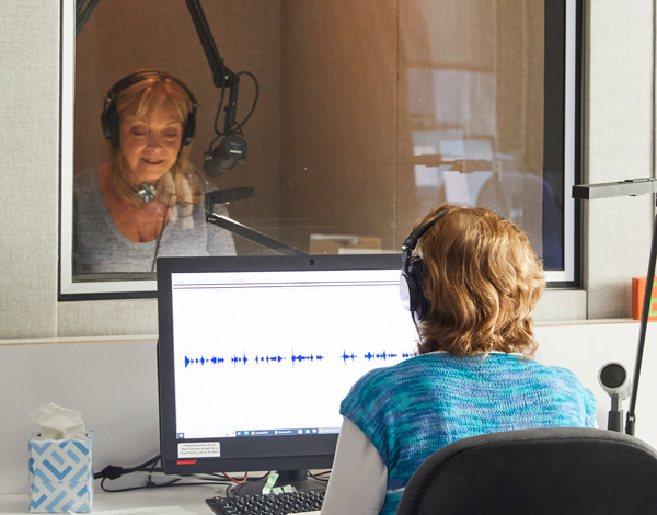 Image: A pair of JBI volunteers, one recording at the microphone, and the other directing
